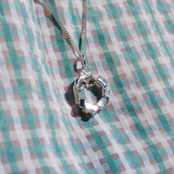 Silverhalsband Pussel av smyckesdesigner Tove Guander, hängandes över rutigt tyg.